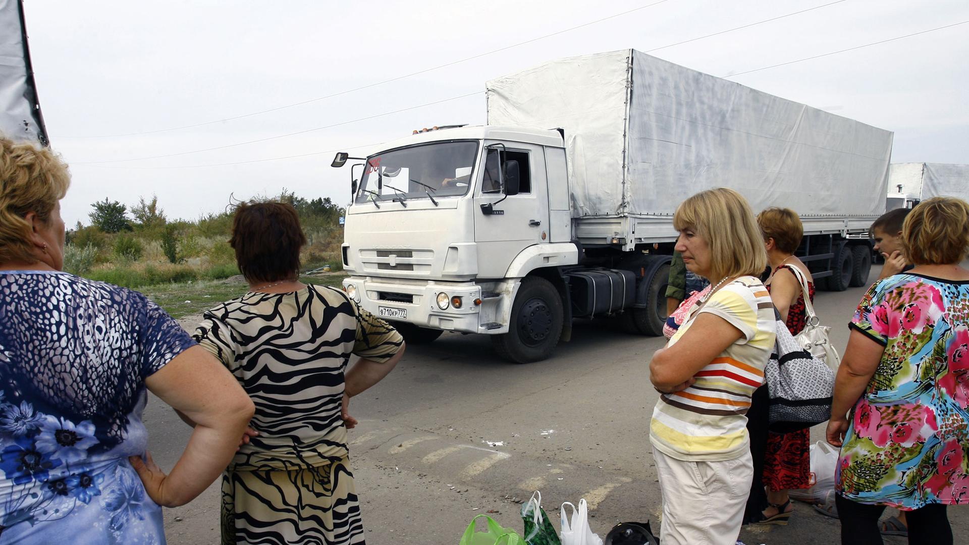 Eine Gruppe von Menschen mit Tüten und Taschen schaut auf die Lkw, die zu dem russischen Hilfskonvoi gehören und auf die Freigabe warten, die Grenze zur Ukraine überqueren zu dürfen. Eine Gruppe von Menschen mit Tüten und Taschen schaut auf die Lkw, die zu dem russischen Hilfskonvoi gehören und auf die Freigabe warten, die Grenze zur Ukraine überqueren zu dürfen.