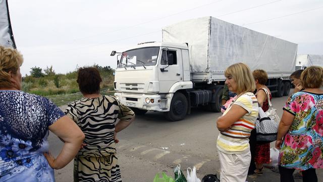 Eine Gruppe von Menschen mit Tüten und Taschen schaut auf die Lkw, die zu dem russischen Hilfskonvoi gehören und auf die Freigabe warten, die Grenze zur Ukraine überqueren zu dürfen.