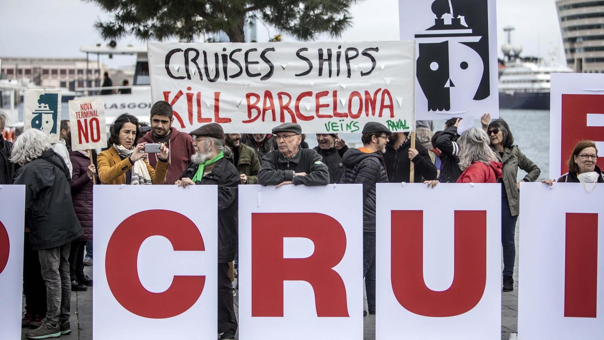 Demonstranten halten Banner hoch auf denen steht, dass die Kreuzfahrtschiffe "Barcelona töten".