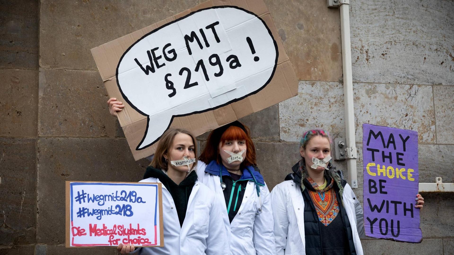 Drei Frauen halten auf einer Demo in Berlin Schilder in die Höhe, auf der sie gegen den Paragraf 219a protestieren. Drei Frauen halten auf einer Demo in Berlin Schilder in die Höhe, auf der sie gegen den Paragraf 219a protestieren.