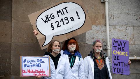Drei Frauen halten auf einer Demo in Berlin Schilder in die Höhe, auf der sie gegen den Paragraf 219a protestieren.