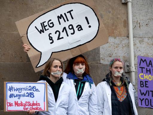 Drei Frauen halten auf einer Demo in Berlin Schilder in die Höhe, auf der sie gegen den Paragraf 219a protestieren.