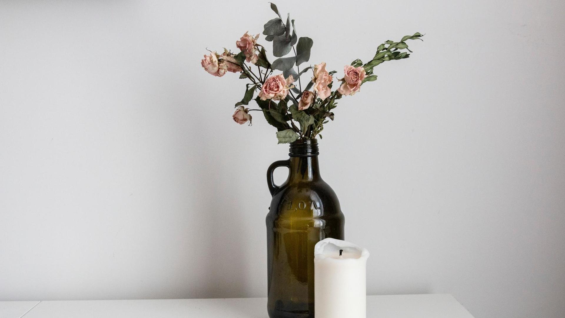 Eine Vase mit einer vertrockneten Rose und eine Kerze stehen auf einem Tisch.