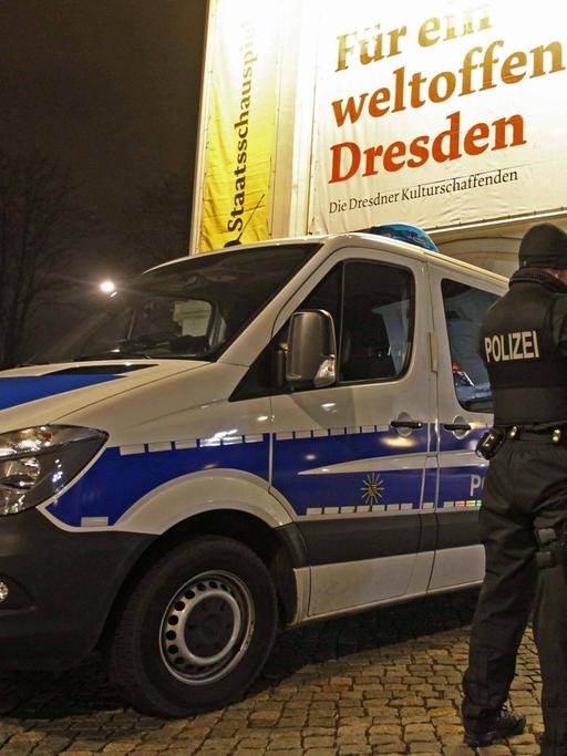 Drei Polizisten stehen in Dresden neben ihrem Einsatzwagen. 
