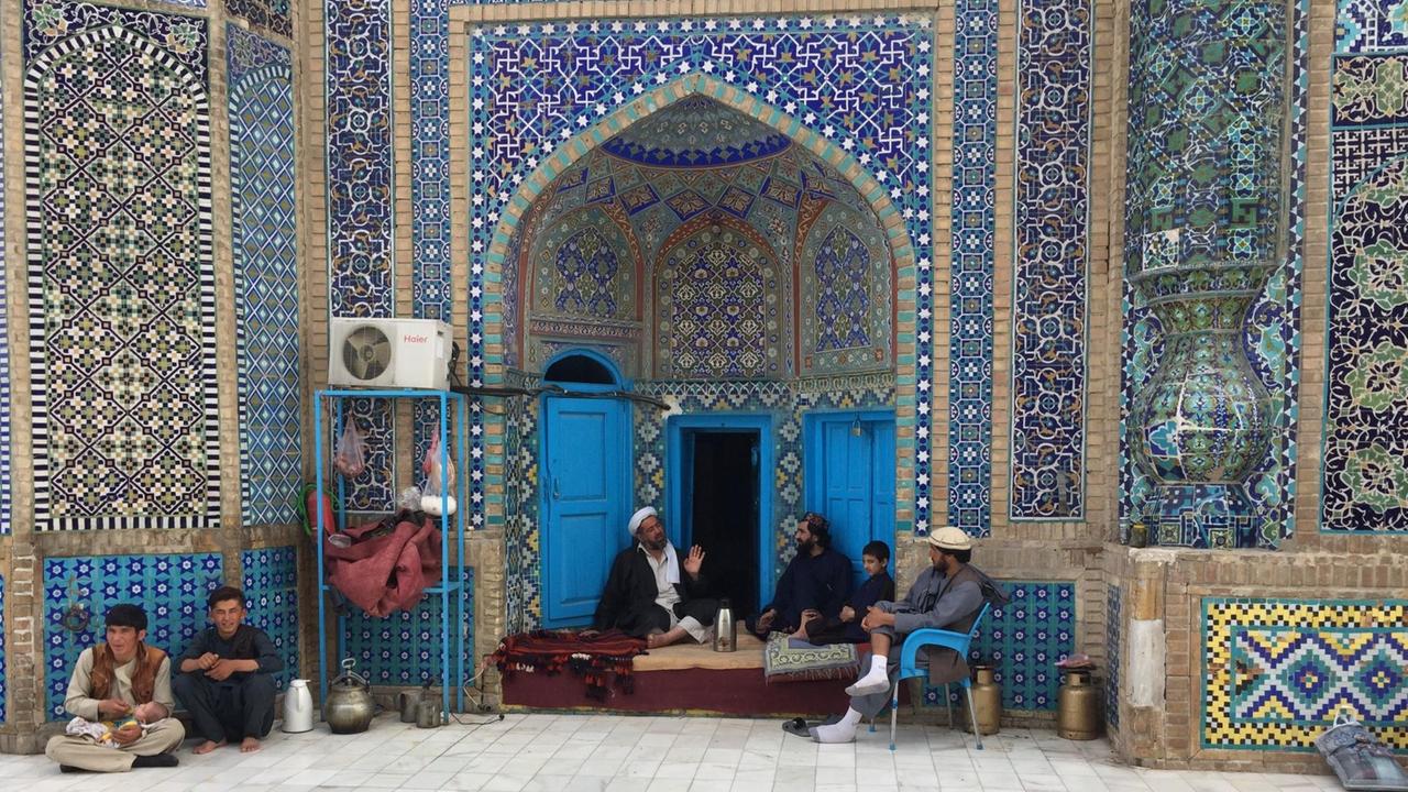 In der Blauen Moschee in Mazar-e Sharif sitzen einige Männer auf Sitzkissen oder dem Boden. Die Wände der Moschee sind mit blauen Kacheln gefliest. In der Blauen Moschee in Mazar-e Sharif sitzen einige Männer auf Sitzkissen oder dem Boden. Die Wände der Moschee sind mit blauen Kacheln gefliest.