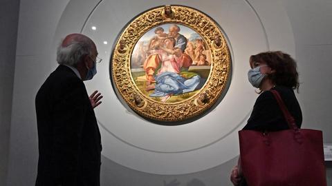 Ein Mann und eine Frau, beide tragen einen Mund-Nase-Schutz, stehen vor dem runden Gemälde "Tondo Doni" von Michelangelo in den Uffizien in Venedig. Es zeigt Maria, Joseph und das Christuskind.
