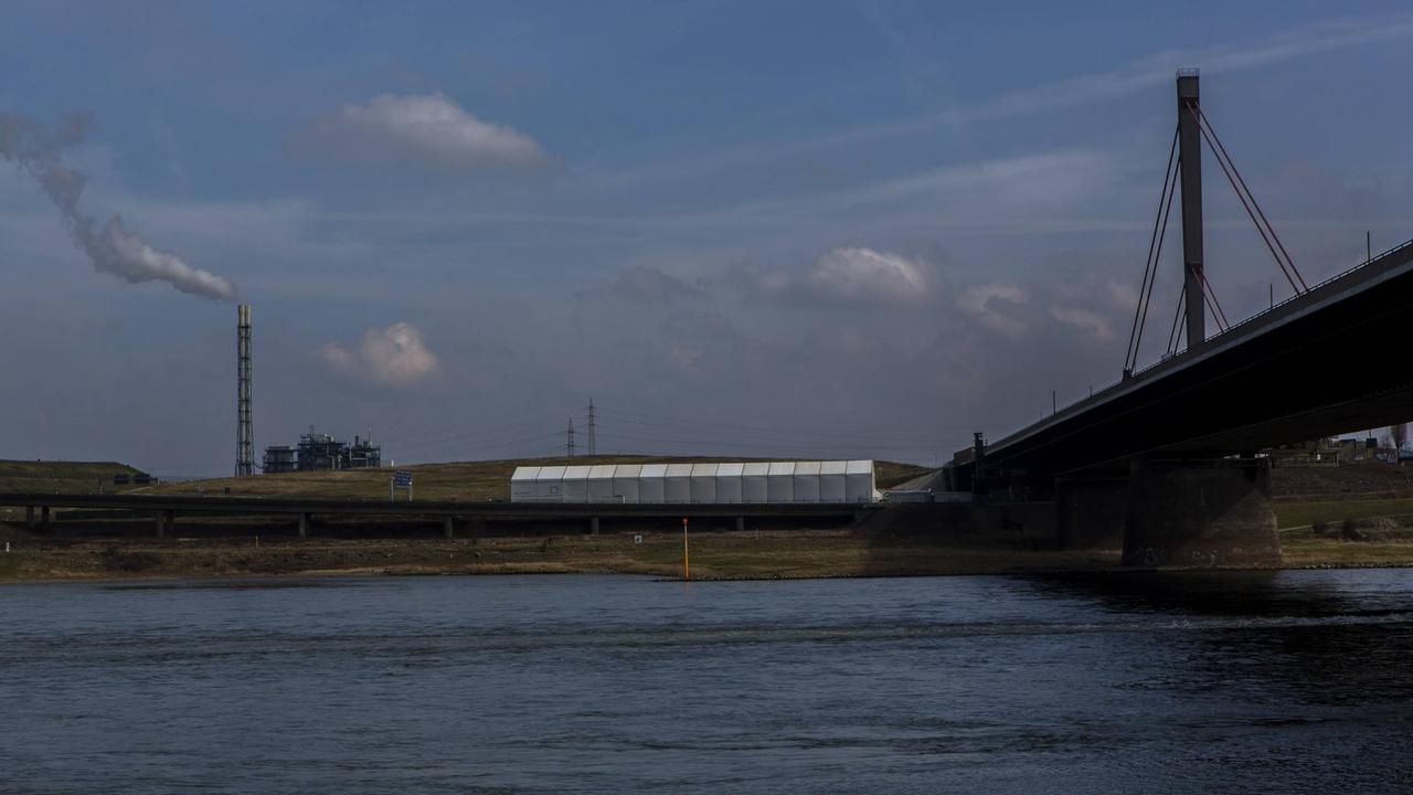 Blick auf den Rhein und dahinter die Grabungsstelle an der Deponie Dhünnaue, die von einem langgestreckten weißen Zeltbau abgedeckt ist. Blick auf den Rhein und dahinter die Grabungsstelle an der Deponie Dhünnaue, die von einem langgestreckten weißen Zeltbau abgedeckt ist.