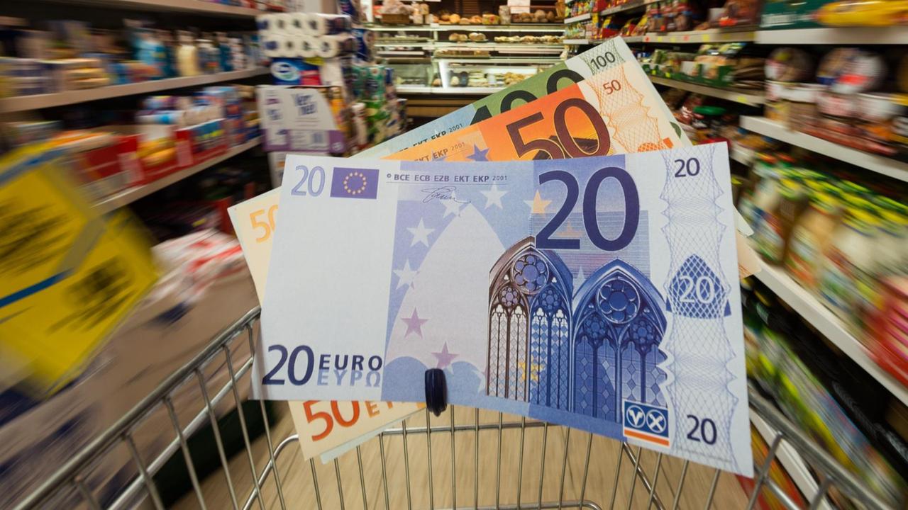 Überdimensionale Geldscheine in einem Einkaufswagen werden durch einen Supermarkt geschoben. Überdimensionale Geldscheine in einem Einkaufswagen werden durch einen Supermarkt geschoben.