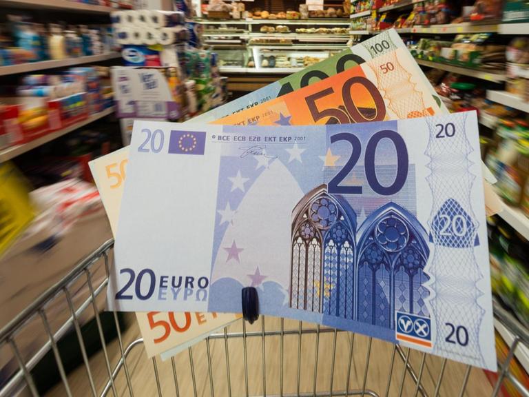 Überdimensionale Geldscheine in einem Einkaufswagen werden durch einen Supermarkt geschoben.