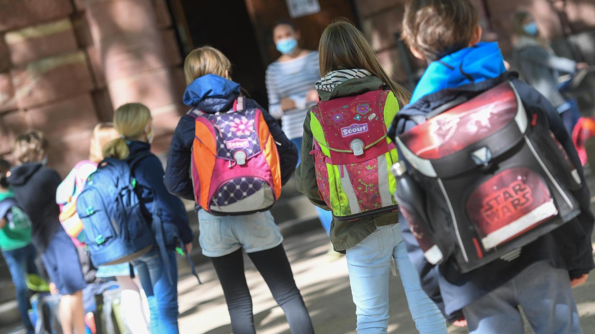 Mehrere Schulkinder mit Ranzen auf den Rücken gehen auf ihre Lehrerin zu. Mehrere Schulkinder mit Ranzen auf den Rücken gehen auf ihre Lehrerin zu.