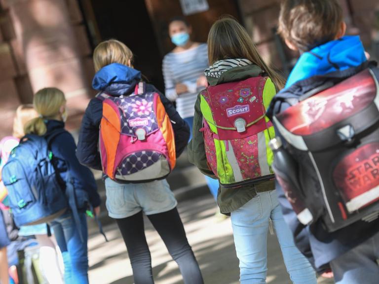 Frankfurt am Main: Schülerinnen und Schüler einer vierten Klasse der Linnéschule werden auf dem Schulhof von ihrer Klassenlehrerin begrüßt, die einen Mundschutz trägt.