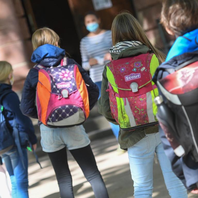 Frankfurt am Main: Schülerinnen und Schüler einer vierten Klasse der Linnéschule werden auf dem Schulhof von ihrer Klassenlehrerin begrüßt, die einen Mundschutz trägt.