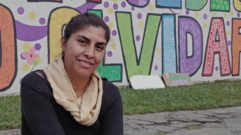 Mayra Rodriguez sitzt vor einer Mauer mit Gaffiti. Mayra Rodriguez sitzt vor einer Mauer mit Gaffiti.