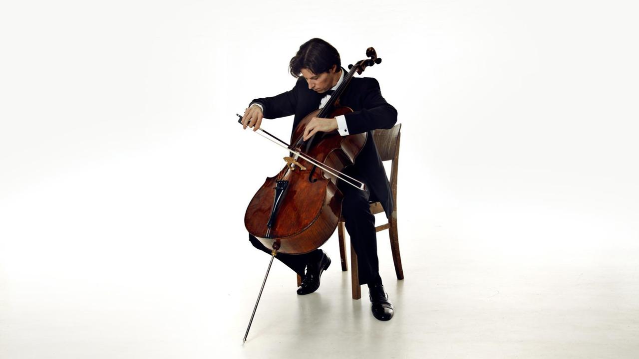Ein Mann in Anzug sitzt mit seinem Cello in einem weißen Raum Ein Mann in Anzug sitzt mit seinem Cello in einem weißen Raum