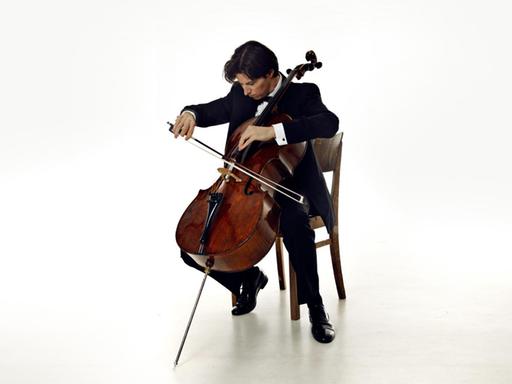 Ein Mann in Anzug sitzt mit seinem Cello in einem weißen Raum