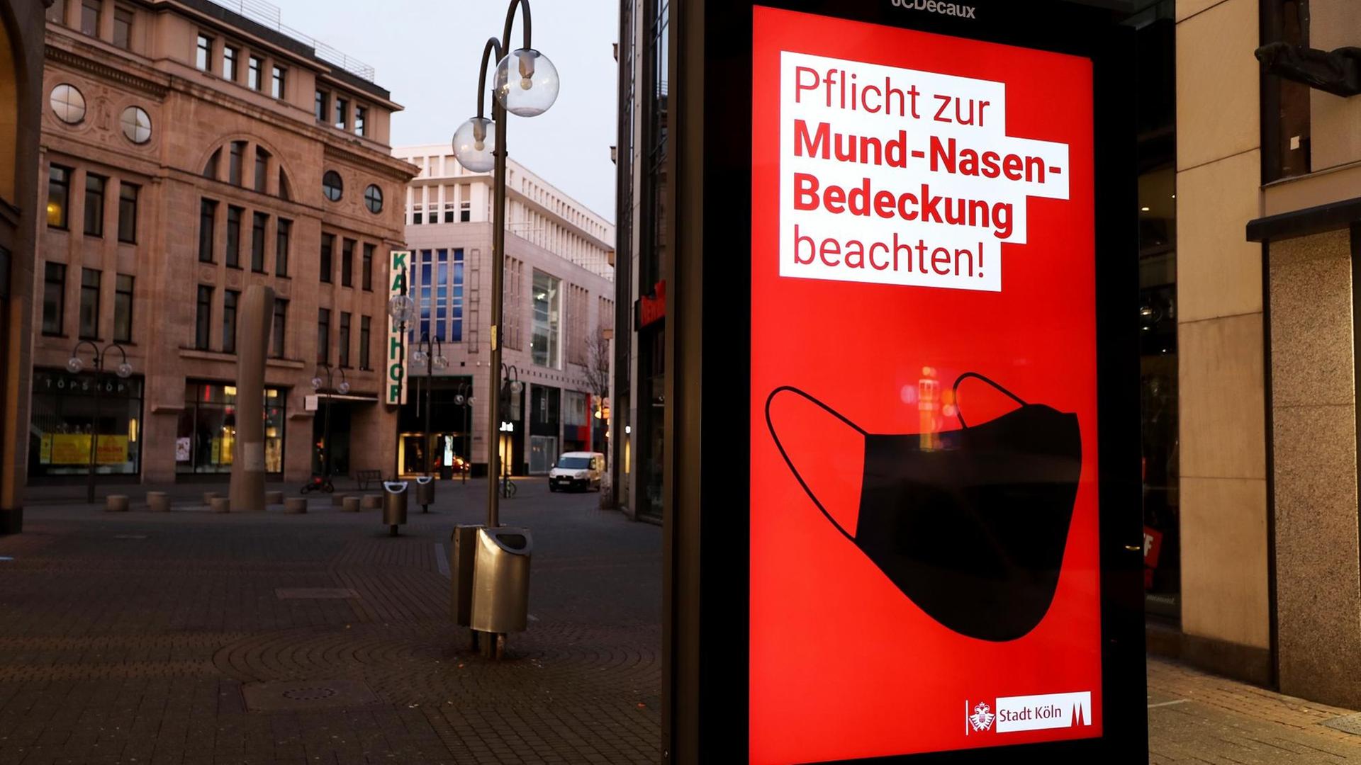 Eine Anzeigetafel weist in der Fußgängerzone von Köln auf die Maskenpflicht hin