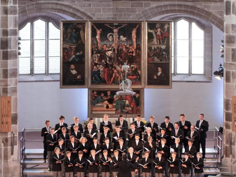 Ein Knabenchor steht im Altarraum einer großen Kirche und singt.