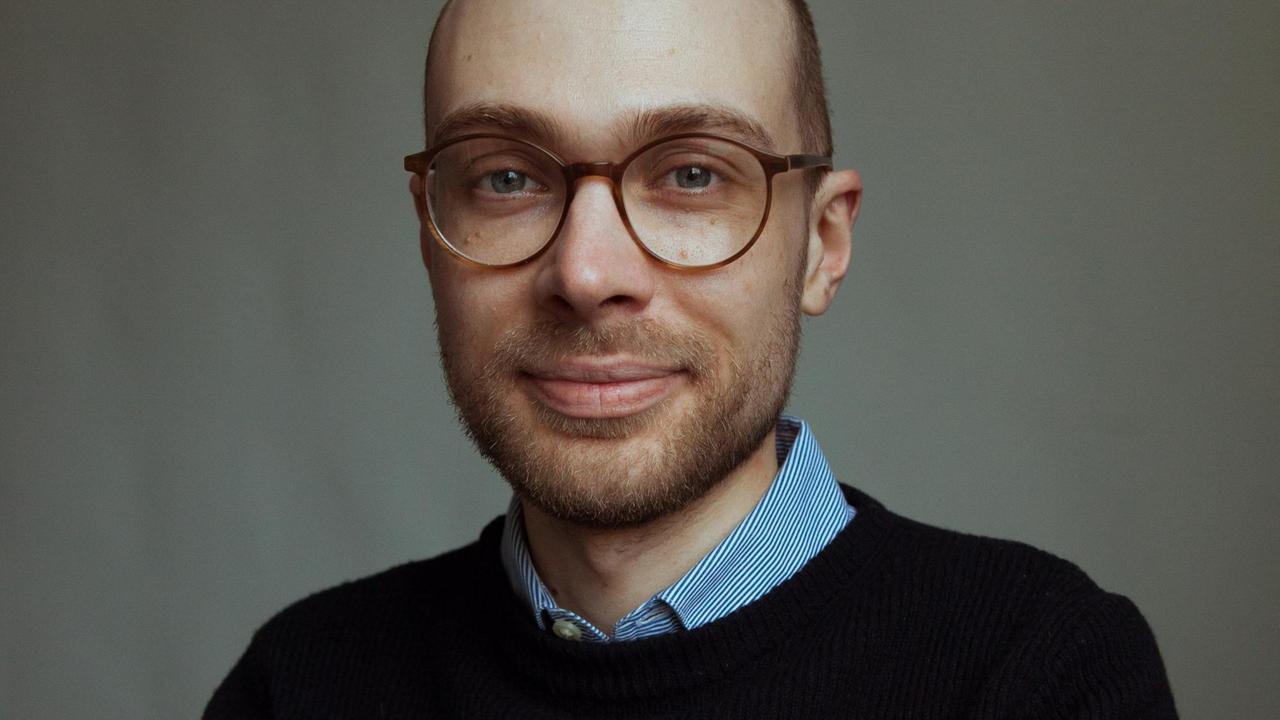 Simon Schwartz trägt Brille und Bar und schaut freundlich in die Kamera. Simon Schwartz trägt Brille und Bar und schaut freundlich in die Kamera.