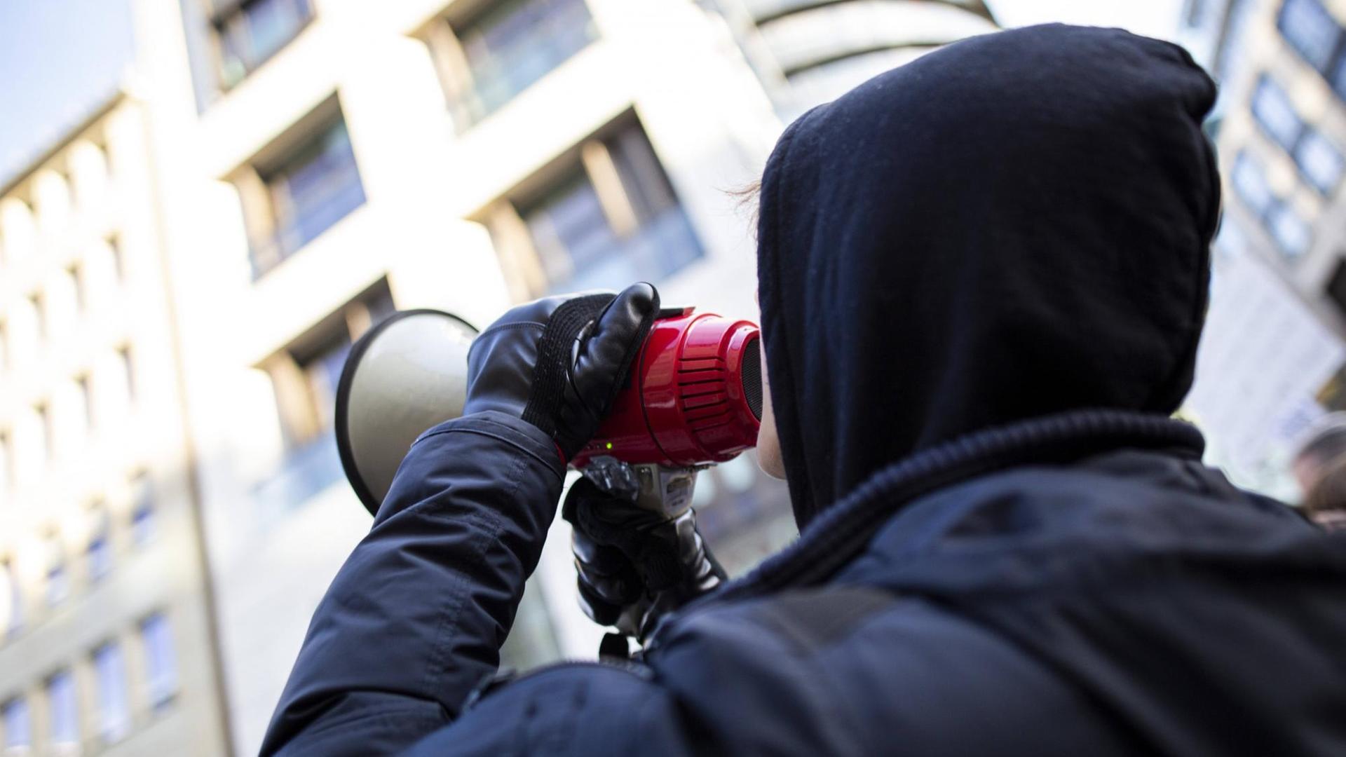 Ein junger Mann trägt Kapuzenpulli und ruft in ein Megaphon Ein junger Mann trägt Kapuzenpulli und ruft in ein Megaphon