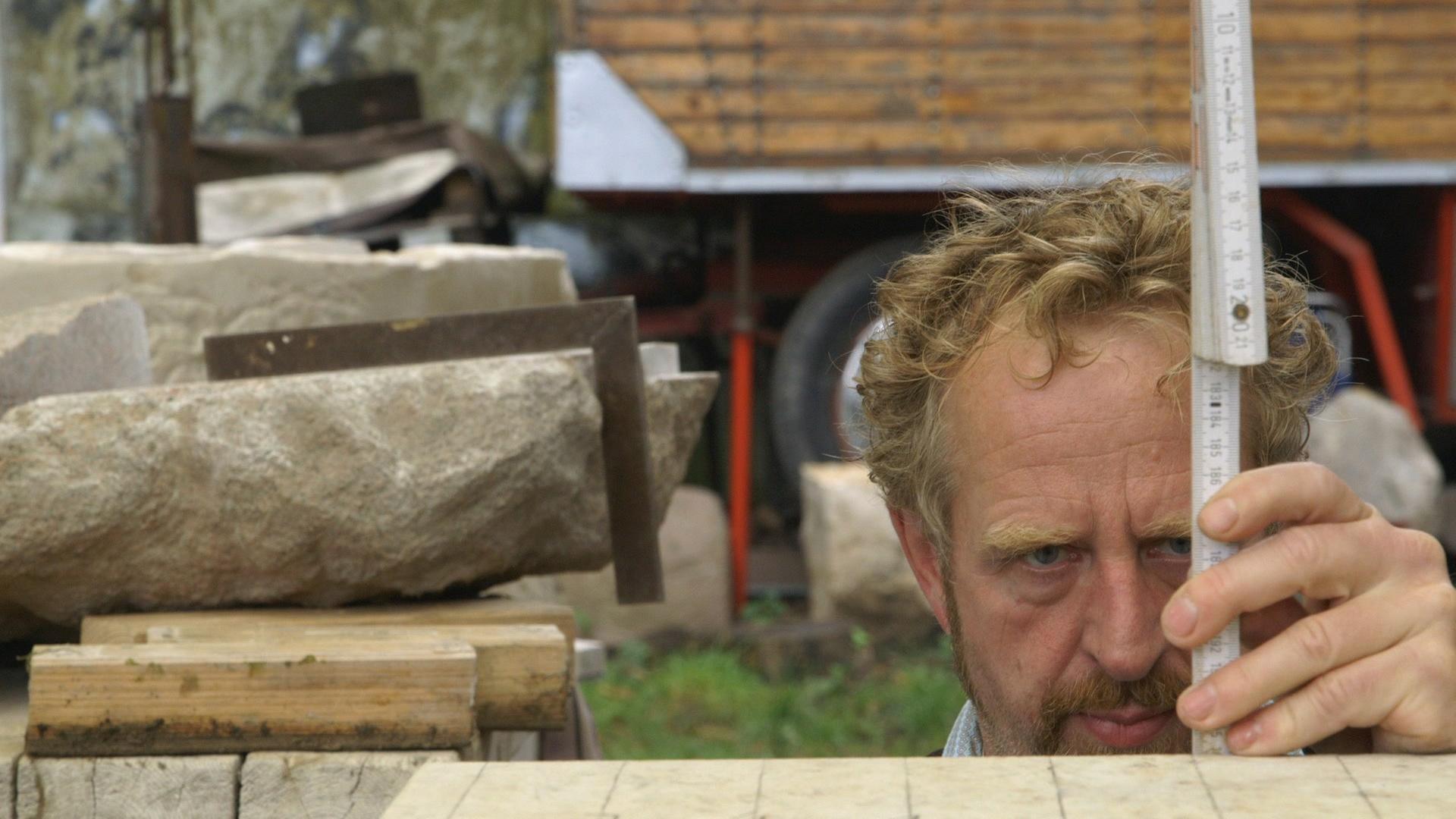 Auf dem Bild ist der Steinmetz Michael Spengler bei der Arbeit zu sehen. Aufmerksam misst er einen Stein mit einem Zollstock ab. Auf dem Bild ist der Steinmetz Michael Spengler bei der Arbeit zu sehen. Aufmerksam misst er einen Stein mit einem Zollstock ab.