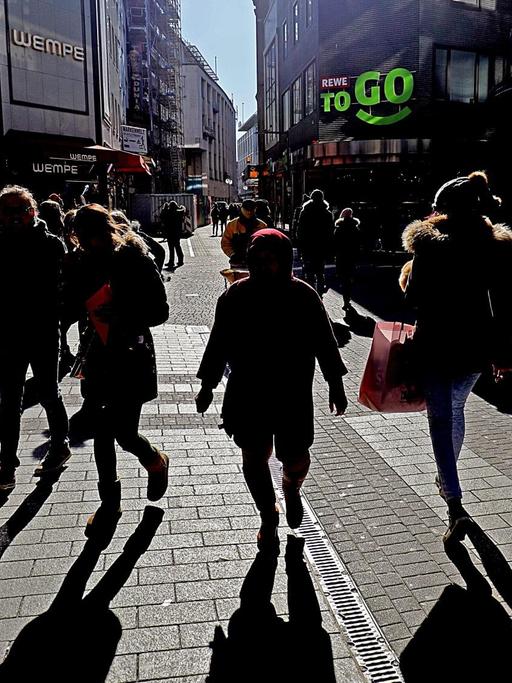 Menschen in der Fußgängerzone "Hohe Straße" in Köln werfen in der Mittagssonne lange Schatten.