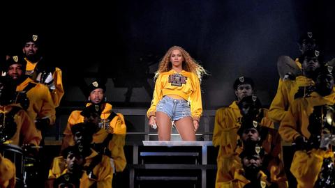Beyoncé steht in abgerissenen Jeans und einem knallgelben Pullover auf der Bühne und schaut ins Publikum.