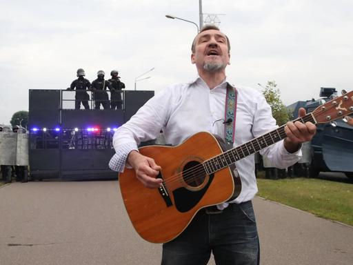 Der Gitarrist Pit Pawlow der belarussischen Band "N.R.M." steht mit einer Gitarre vor einer Polizeibarrikade.
