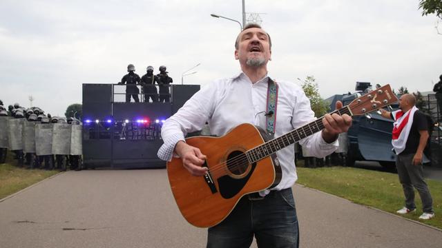 Der Gitarrist Pit Pawlow der belarussischen Band "N.R.M." steht mit einer Gitarre vor einer Polizeibarrikade.