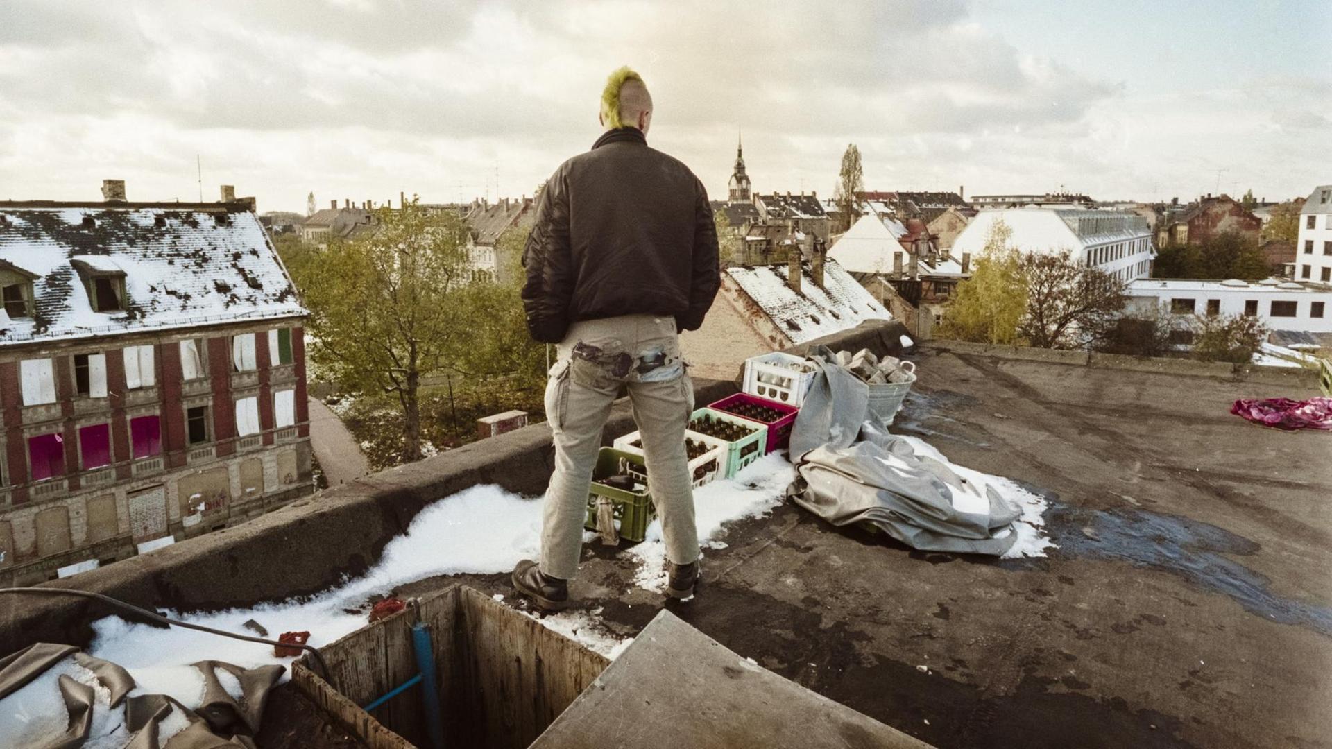 Ein junger Mann mit Irokesenschnitt steht auf dem Dach eines besetzten Hauses und schaut auf das Leipziger Szeneviertel Connewitz. Ein junger Mann mit Irokesenschnitt steht auf dem Dach eines besetzten Hauses und schaut auf das Leipziger Szeneviertel Connewitz.