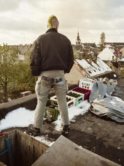 Ein junger Mann mit Irokesenschnitt steht auf dem Dach eines besetzten Hauses und schaut auf das Leipziger Szeneviertel Connewitz.