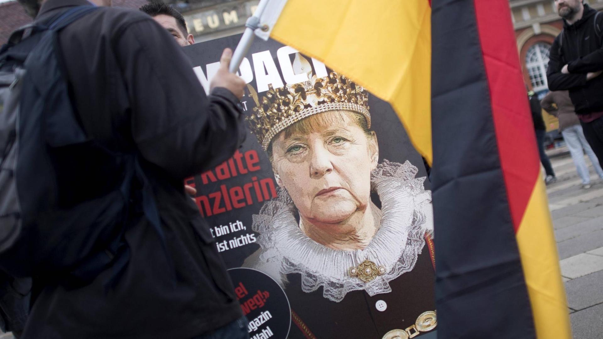 Auf einer Demonstration ist ein Anti-Merkel-Plakat zu sehen, im Vordergrund eine Deutschland-Flagge. Auf einer Demonstration ist ein Anti-Merkel-Plakat zu sehen, im Vordergrund eine Deutschland-Flagge.