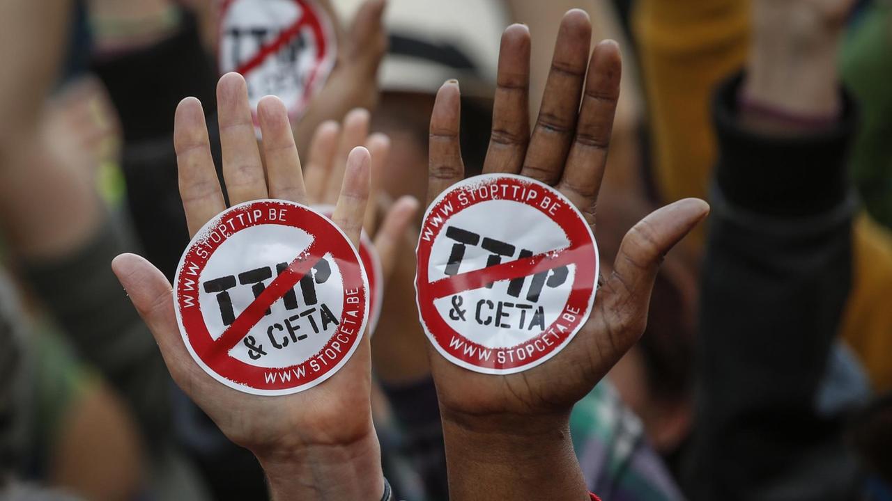 Zwei Gegner der Freihandelsabkommen TTIP und CETA zeigen jeweils eine Hand, auf der ein Aufkleber mit durchgestrichenem TTIP- und Ceta-Schriftzug prangt.