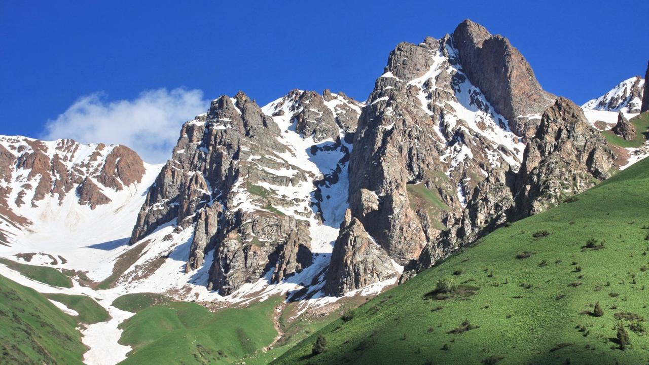 Kirgisistan ist zu etwa einem Drittel von Gletschern und ewigen Schneefeldern bedeckt. Hohe Berge mit Schnee und darunter grüne Ebenen sind zu sehen.