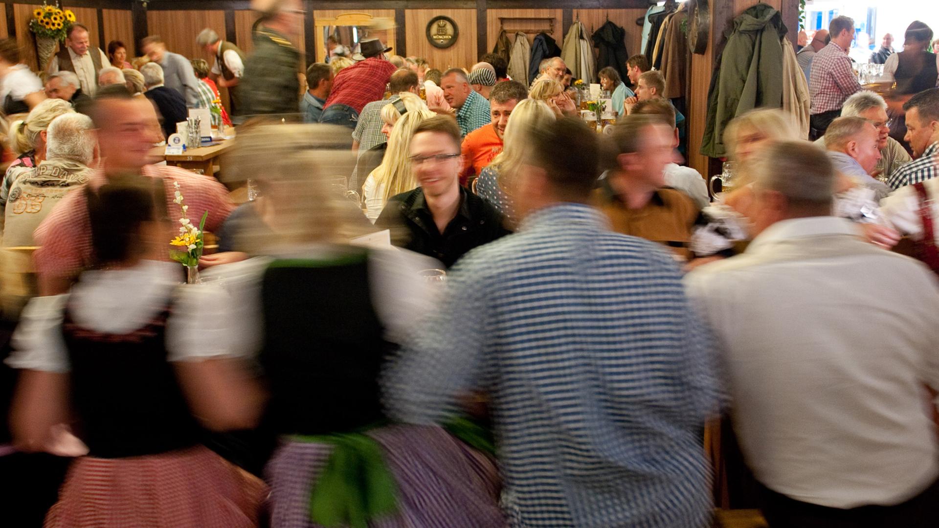 Menschen sitzen um Tische auf Bänken und Schunkeln, Frauen tragen Dirndl Menschen sitzen um Tische auf Bänken und Schunkeln, Frauen tragen Dirndl