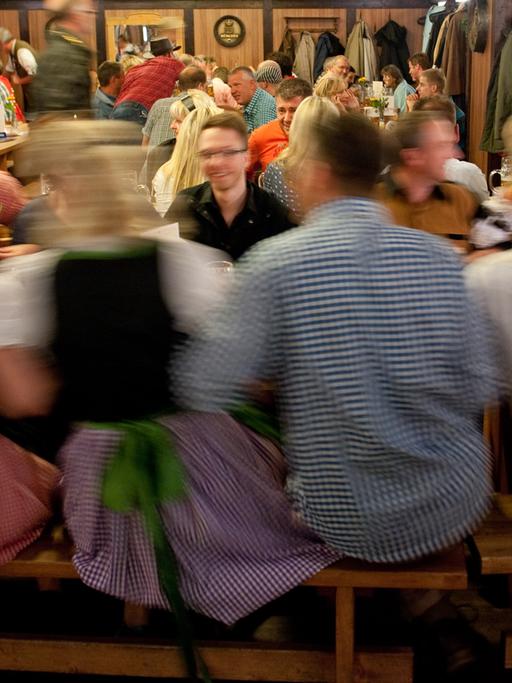 Menschen sitzen um Tische auf Bänken und Schunkeln, Frauen tragen Dirndl