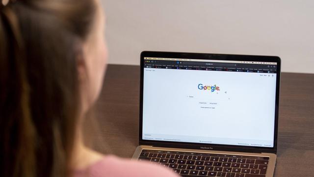 Eine Frau sitzt vor einem Laptop und sieht sich die Internetseite von Google an.
