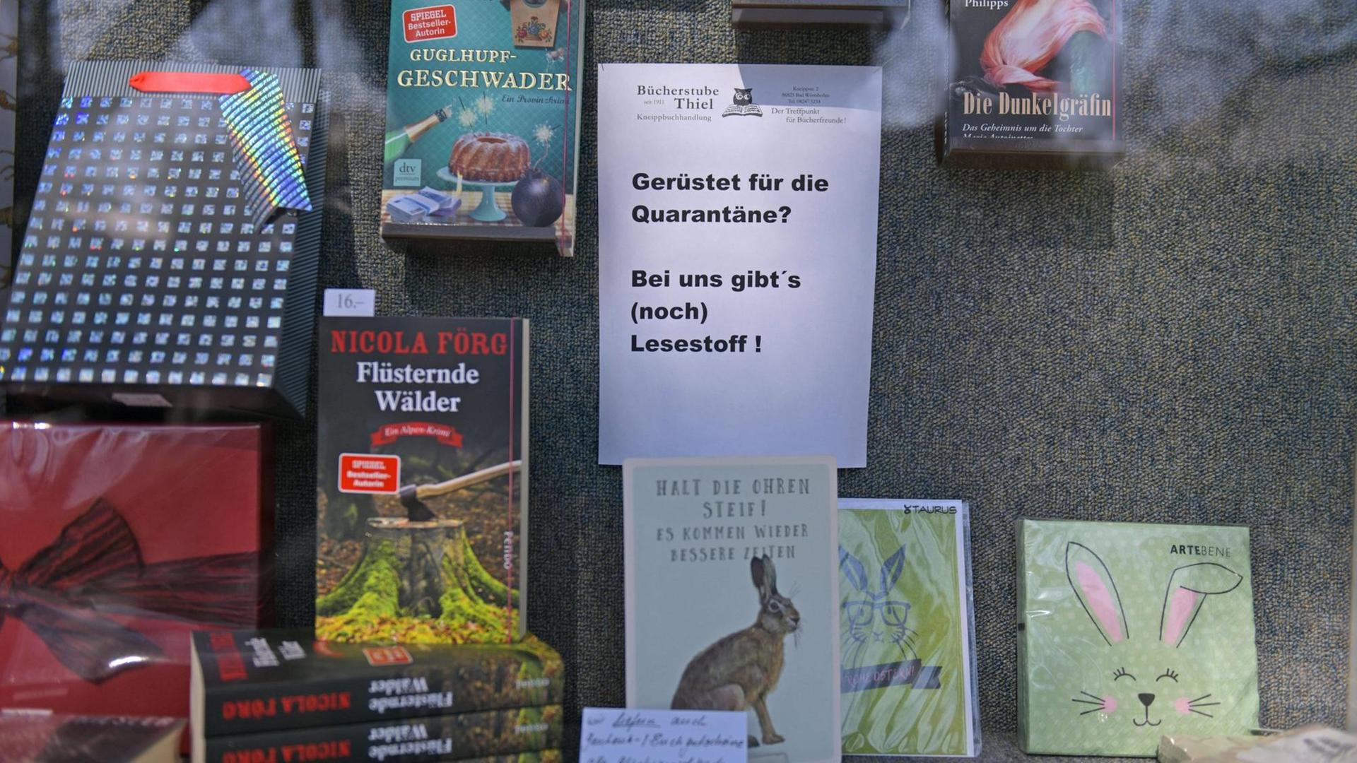Ausschnitt eines Schaufensters einer Buchhandlung in Bayern: Zu sehen sind verschiedene Bücher, dazwischen ein Schild mit der Aufschrift "Gerüstet für die Quarantäne? Bei uns gibt es (noch) Lesestoff!"