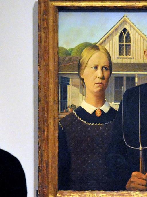 Grant Woods "American Gothic": Ein Bauernpaar vor einem Holzhaus. Ein Mann mit Brille und Mistgabel in der Hand. Daneben eine konservativ gekleidete Frau.