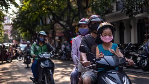 Eine Familie mit Gesichtsmasken auf einem Motorroller in der vietnamesischen Hauptstadt Hanoi.