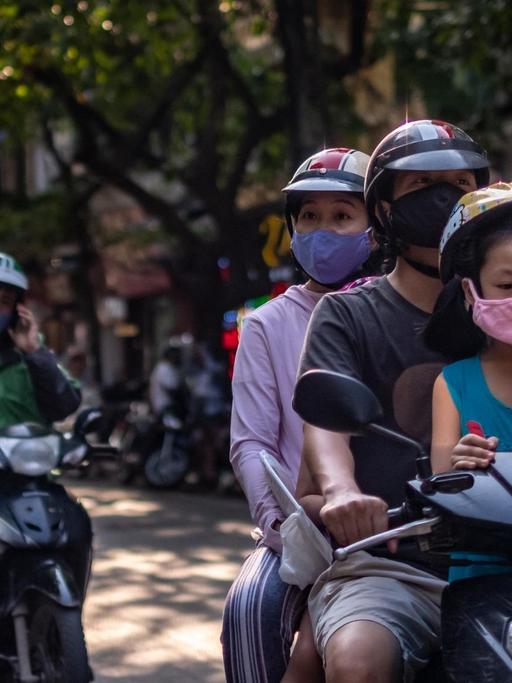 Eine Familie mit Gesichtsmasken auf einem Motorroller in der vietnamesischen Hauptstadt Hanoi.