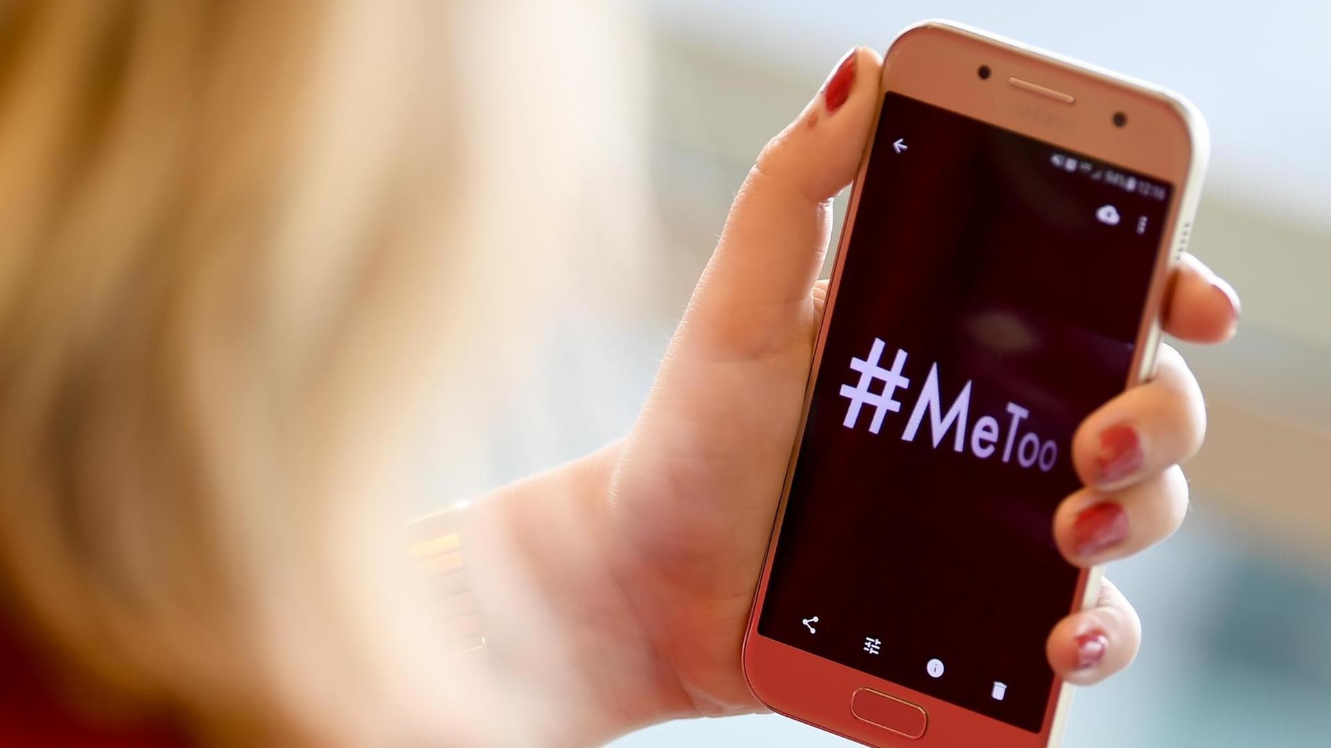 Eine Frau schaut auf ein Smartphone-Display auf dem das Hashtag #MeToo steht.