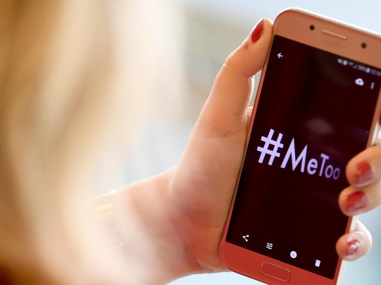 Eine Frau schaut auf ein Smartphone-Display auf dem das Hashtag #MeToo steht.