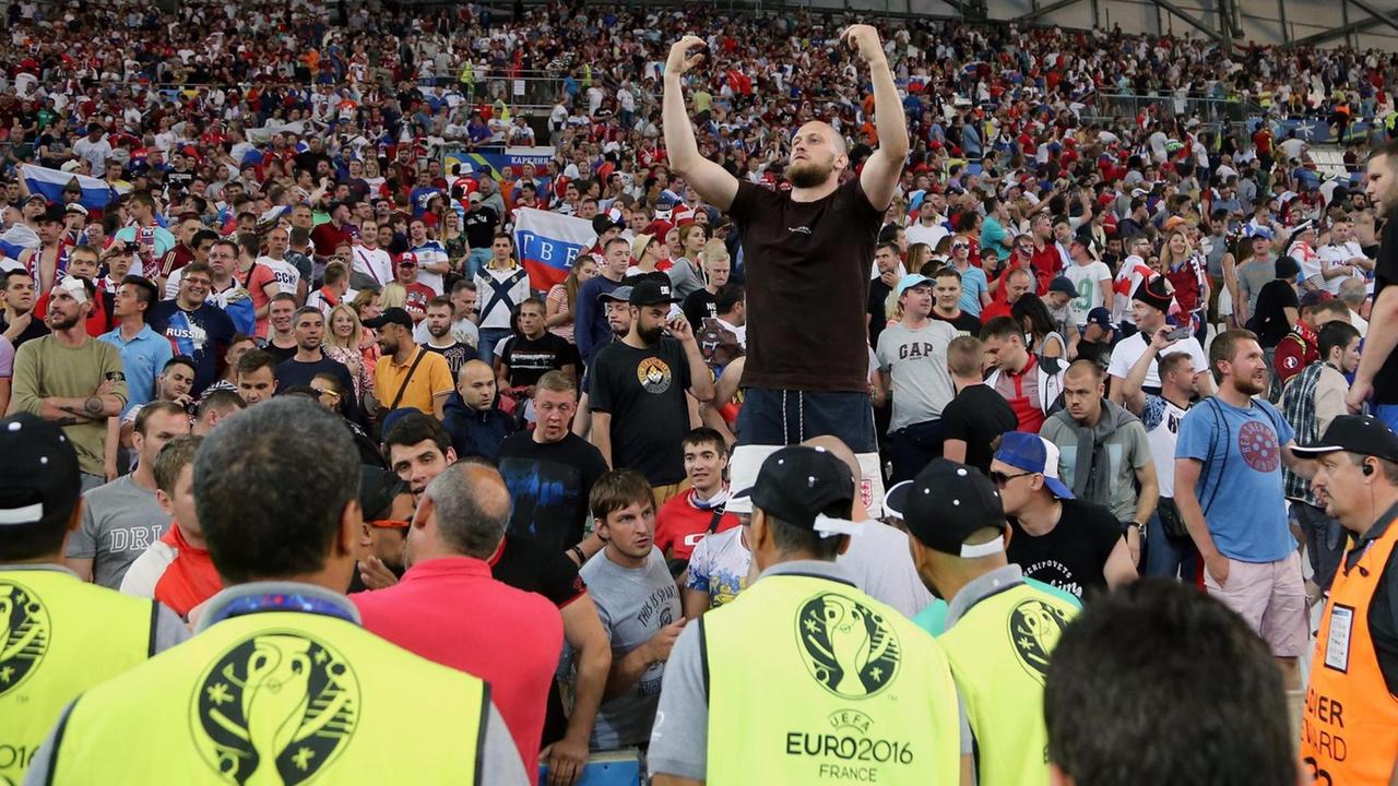 Ordner in leuchtgelben Warnwesten stehen vor einer Tribüne voller Zuschauer. Ordner in leuchtgelben Warnwesten stehen vor einer Tribüne voller Zuschauer.