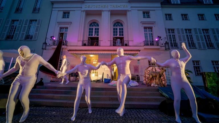 Vier in silberfarbene Latex-Anzüge gekleidete Menschen rennen die Treppe vom Deutschen Theater herunter und halten sich dabei an den Händen. Vier in silberfarbene Latex-Anzüge gekleidete Menschen rennen die Treppe vom Deutschen Theater herunter und halten sich dabei an den Händen.