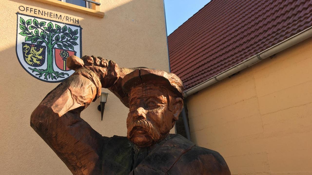 Der holzgeschnitzte Gemeindebote von Offenheim vor einer Hauswand mit dem Ortswappen. Der holzgeschnitzte Gemeindebote von Offenheim vor einer Hauswand mit dem Ortswappen.