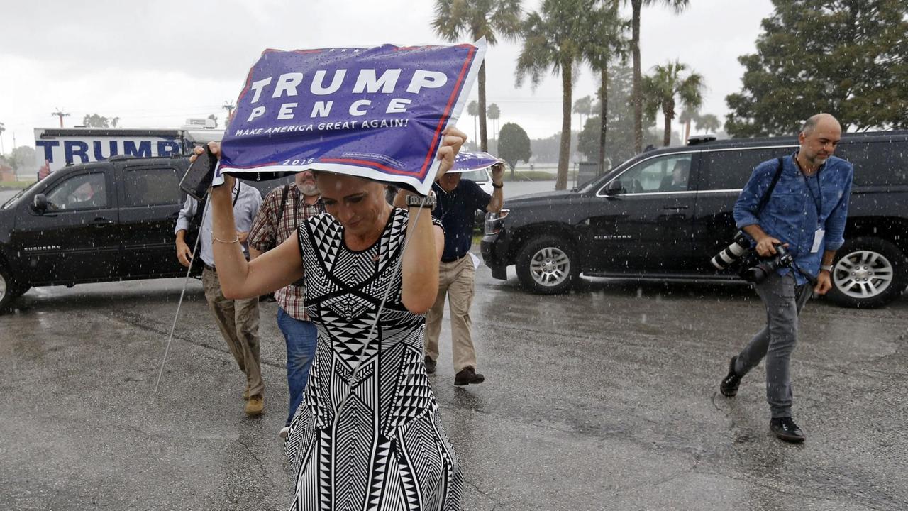 Stephanie Grisham steht bei einer Wahlkampfrally in Tampa im Regen und schützt sich mit einem Wahlkampf-Banner vor der Nässe. 