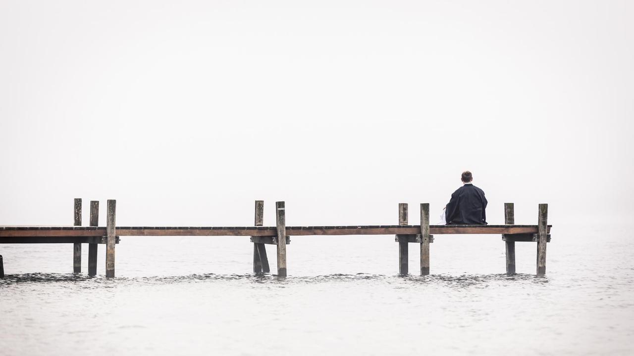Ein Mann sitzt einsam an einem Bootssteg.