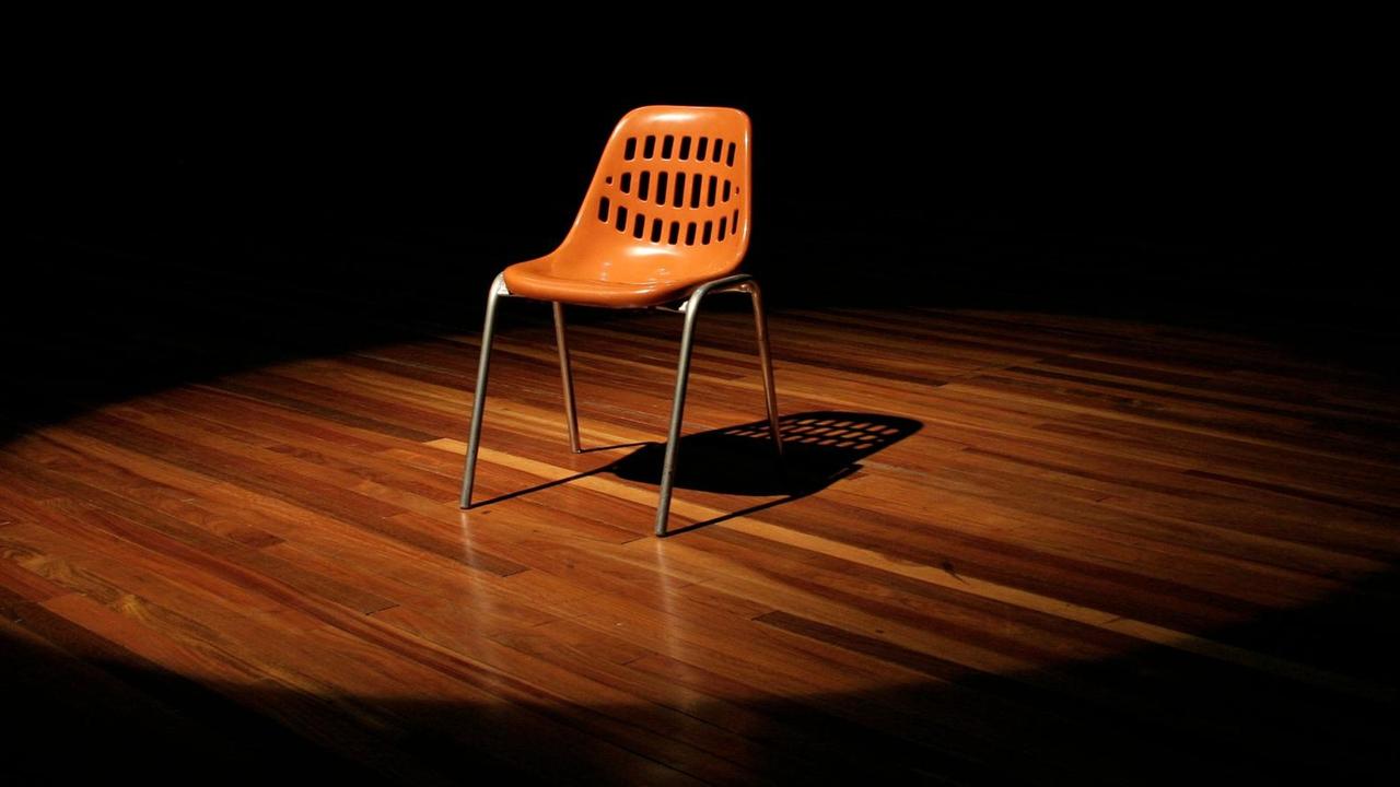 Ein leerer Stuhl steht auf einer Theaterbühne. Ein leerer Stuhl steht auf einer Theaterbühne.