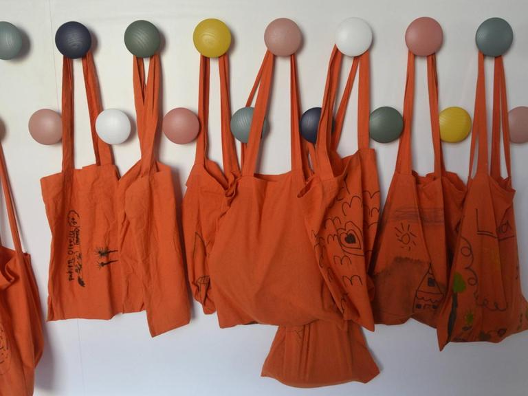 An bunten Haken hängen orangefarbene Stoffbeutel.