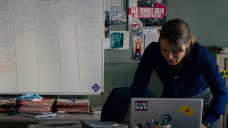 Ein Screenshot aus der Polizeiruf 110 - Folge "Für Janina": Anneke Kim Sarnau tippt auf ihrem Laptop, auf dem ein "FCK NZS"-Aufkleber und ein Aufkleber der Anti-Atombewegung kleben. Im Hintergrund unter anderem ein Poster mit der Aufschrift "Nazi verpiss Dich". Ein Screenshot aus der Polizeiruf 110 - Folge "Für Janina": Anneke Kim Sarnau tippt auf ihrem Laptop, auf dem ein "FCK NZS"-Aufkleber und ein Aufkleber der Anti-Atombewegung kleben. Im Hintergrund unter anderem ein Poster mit der Aufschrift "Nazi verpiss Dich".